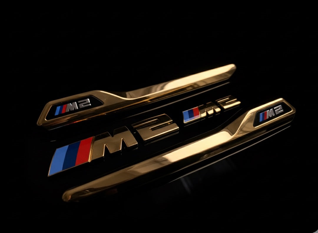 Vergoldetes BMW M2 Emblem mit sichtbaren Kanten und Metallreflexen im Detail