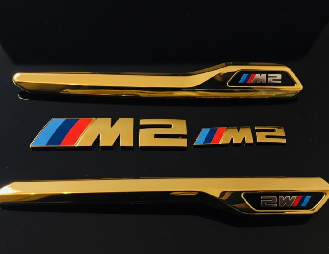 Vergoldete BMW M2 Auto-Embleme und Zierleisten auf schwarzem Untergrund
