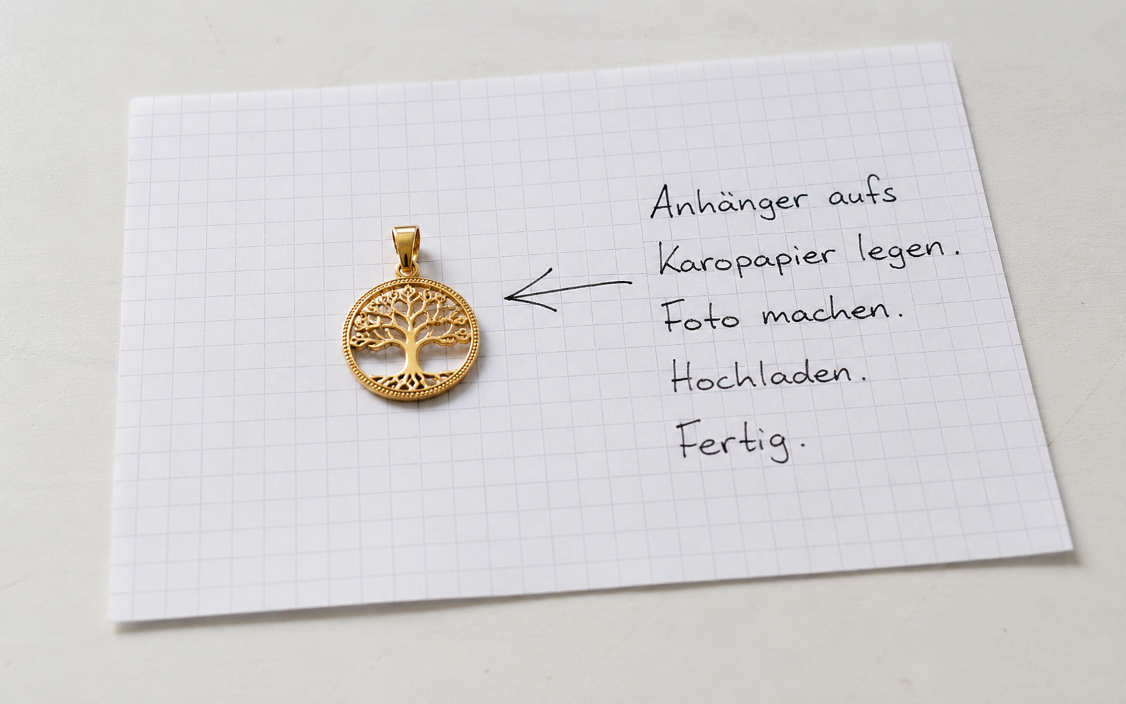 Goldener Anhänger auf Karopapier mit Pfeil und Hinweis zum Foto hochladen
